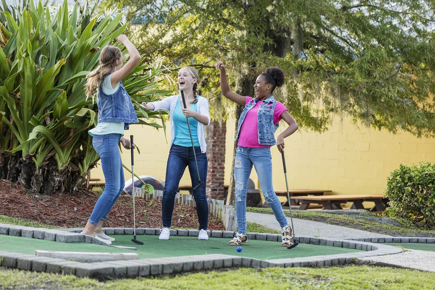 Girl with malformed arm, friends playing miniature golf